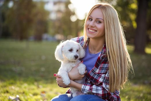 Beautiful woman spending time with her Maltese dog outdoor.