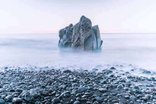 tranquil morning landscape with lonely sea rock on the pebbled shore