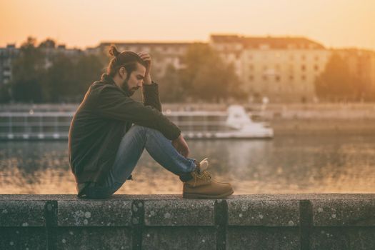 Depressed modern businessman sitting by the river.