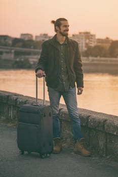 Handsome businessman with suitcase standing by the river.