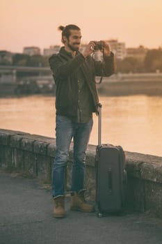 Handsome modern businessman with suitcase enjoys photographing city.