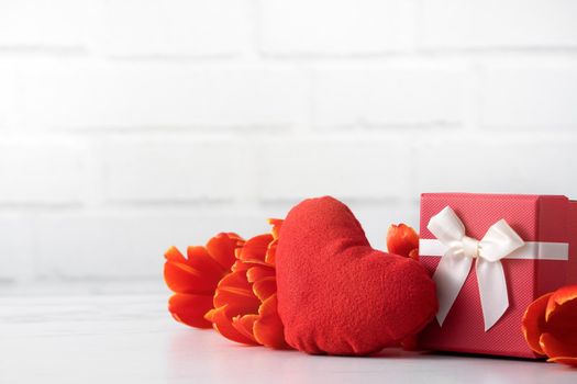 Mother's Day gift. Close up design concept of red tulip bouquet with gift and heart shape on white table background and brick wall decoration.