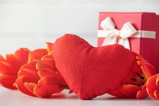 Mother's Day gift. Close up design concept of red tulip bouquet with gift and heart shape on white table background and brick wall decoration.