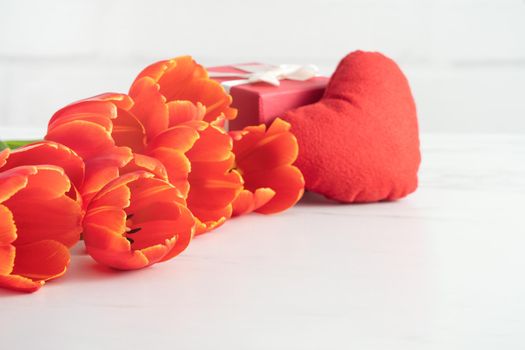 Mother's Day gift. Close up design concept of red tulip bouquet with gift and heart shape on white table background and brick wall decoration.