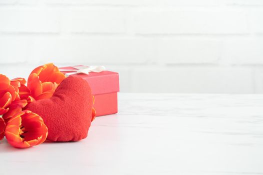Mother's Day gift. Close up design concept of red tulip bouquet with gift and heart shape on white table background and brick wall decoration.