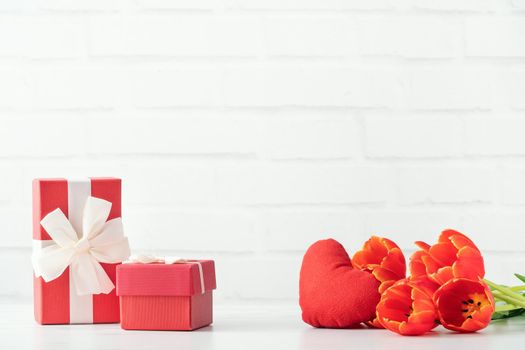 Mother's Day gift. Close up design concept of red tulip bouquet with gift and heart shape on white table background and brick wall decoration.