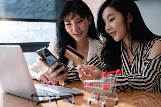 Two young cheerful women in a coffee shop with a credit card and and laptop comfortably buy them over the internet.