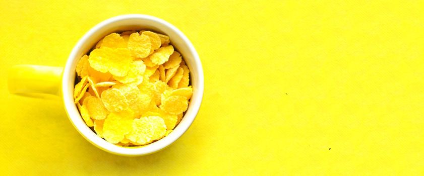 Top view, yellow cup with cornflakes on bright yellow background.