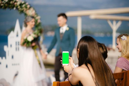 Young girl photographs the bride and groom on a smartphone. Blank screen. High quality photo