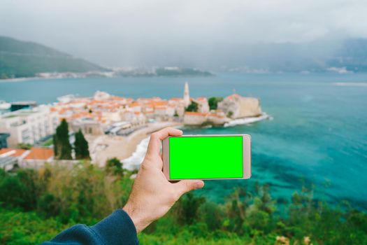 Hand holds a phone with a blank screen. The old town can be seen in the distance. High quality photo