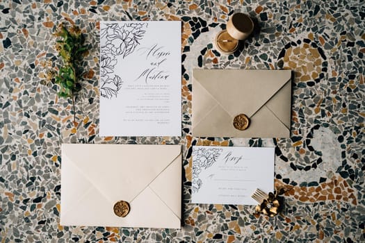 Envelopes and invitations sealed with sealing wax lie on the mosaic tiles. Nearby lies a green twig and a flower-shaped hairpin. High quality photo