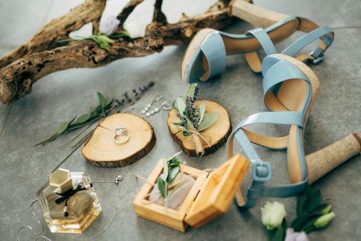 Wedding rings lie in a wooden box surrounded by sandals with heels, perfume, flowers and twigs on the floor. High quality photo
