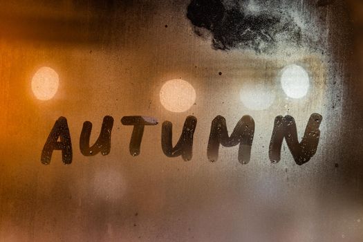 the word autumn handwritten on night wet window glass surface.