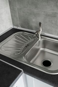 Stainless steel kitchen sink on a dark grey granite worktop. Kitchen sink and water tap in the kitchen