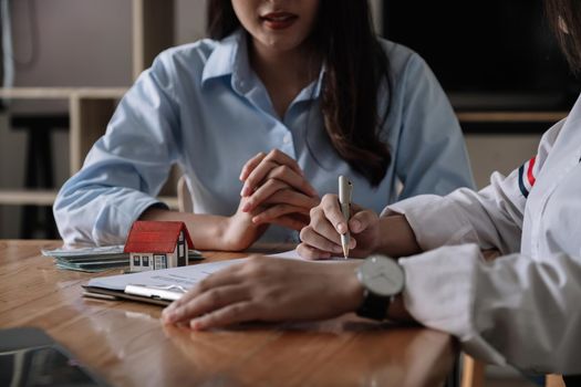 Image of real estate agent assisting client to sign contract paper at desk with house model.