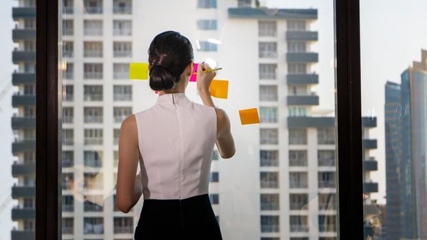 Business woman Write notes on the paper attached to the window glass.