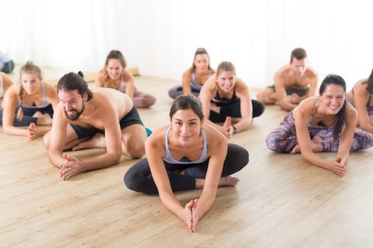 Group of young sporty attractive people in yoga studio, practicing yoga lesson with instructor, sitting on floor in forward band stretching yoga pose. Healthy active lifestyle, working out in gym.