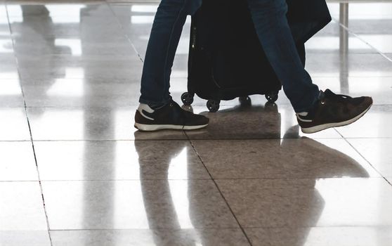 Traveler pulling suitcase in modern airport terminal. Travel and transportation concept