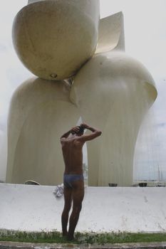 salvador, bahia, brazil - november 13, 2007: homeless man is seen taking a bath next to the sculpture by artist Mario Cravo in the city of Salvador.