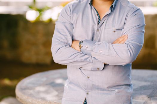 Man in a blue shirt with his arms crossed on his chest leans on a stone table. High quality photo