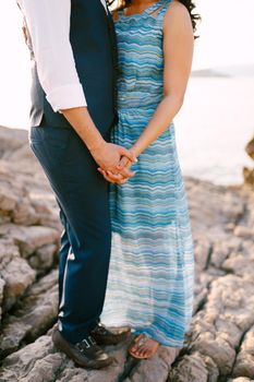 Man in a suit and woman in a long dress with an ornament stand on a stone shore holding hands. High quality photo