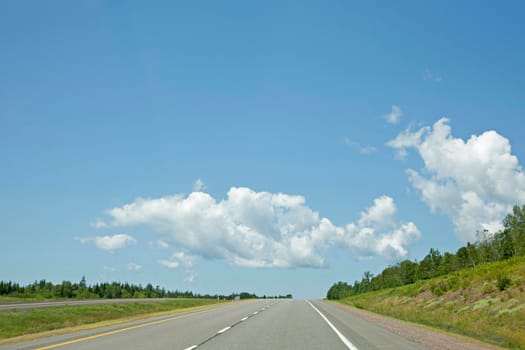 Blue sky and puffy clouds against an empty open highway in the summer