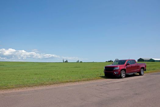 A red pickup truck sits on the side of a rural field road
