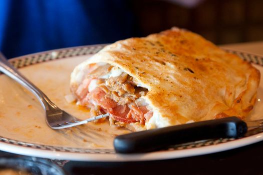 a large sandwich called a calzone with donair meat on a plate with utensils