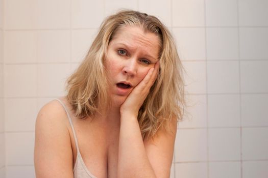  Woman sits in bathroom with hand on face looking sleepy, big yawn 