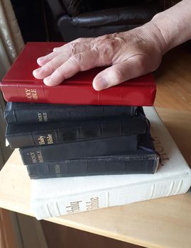  A hand is placed on top of a stack of bibles, ready to swear the truth 