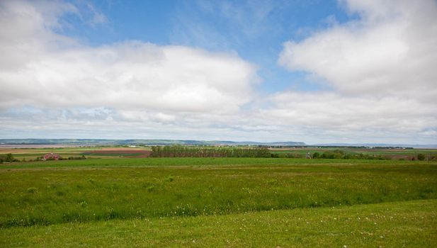 A National Historic Site, the steeple of the Grand Pre Church is just visible in the middle of a meadow, with Cape Blomidon in the background