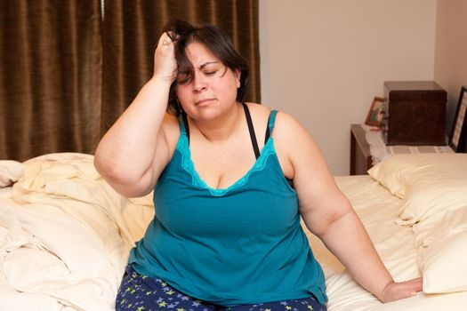 A woman sits on her bedside and holds her head, confused or tired