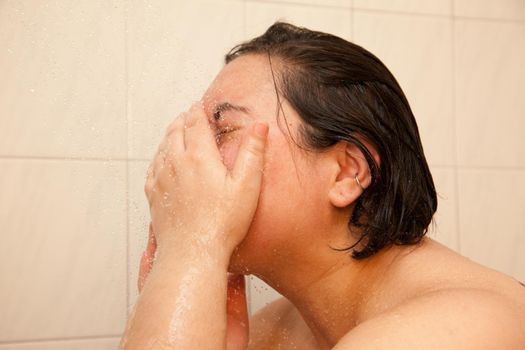 A woman waashes her face under a shower stream 