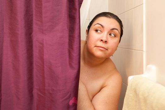  Woman peeks out behind shower curtain curiously 