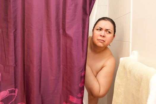 A woman looks out cautiously from behind her shower curtain, concerned she heard a noise