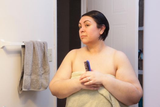 A woman holds her brush, ready to start her morning routine, and looks at her reflection. 