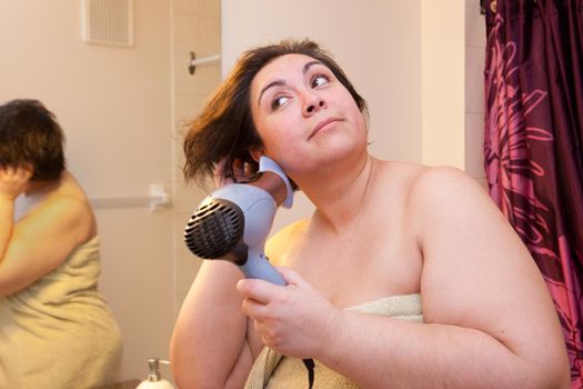 Beautiful woman flips her short hair while using a hairdryer, eyes smiling in the morning. 