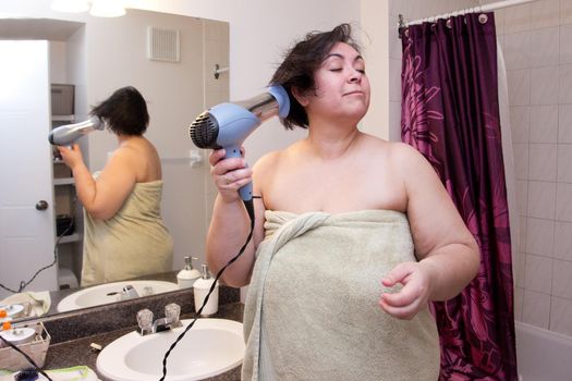 Drying hair wrapped in a towel, a woman stands in her bathroom preparing to go out 
