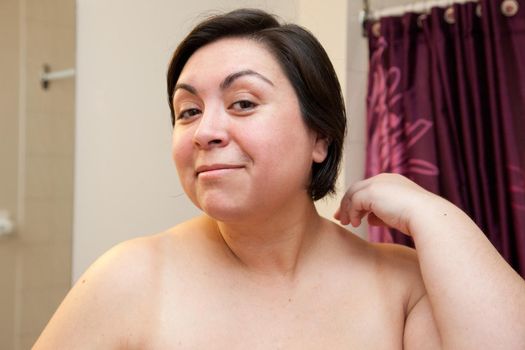 A beautiful curvy model smiles coyly into the camera in bare skin, with no makeup on her face 