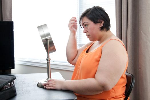 A curvy woman looks at her reflection and hair in a table top mirror