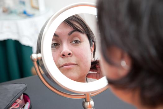 Woman looks at herself in a round dressing table mirror with a natural fresh face 