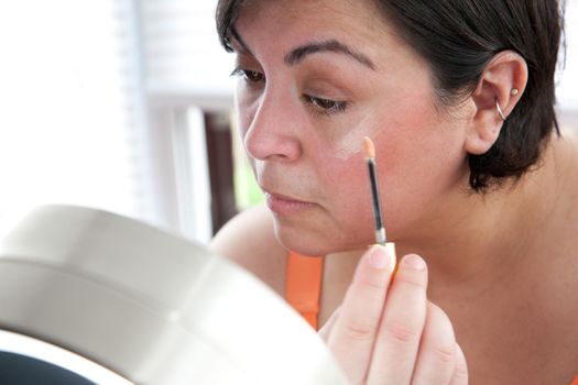 Woman applies cover up or foundation, holding a makeup wand 