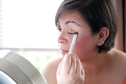 Woman in front of vanity mirror uses a makeup wand to apply eye shadow 