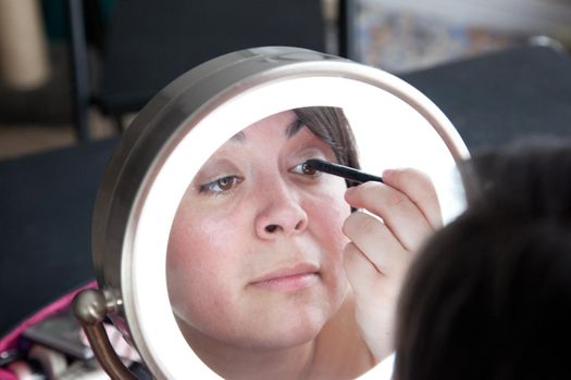 Reflected in a mirror, a woman carefully applies black liner to her eyelid