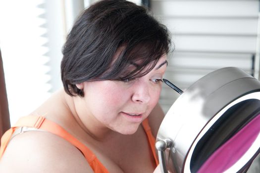 A gorgeous dark haired woman puts on eye liner as part of getting ready routine