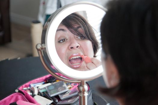  Woman in mirror puts on a shiny pink lip gloss