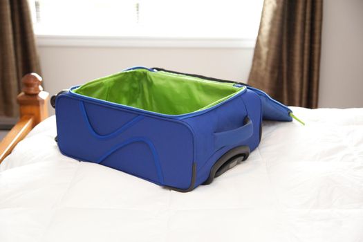 A blue and green unzipped suitcase sits on a bed, ready to be packed for an adventure 