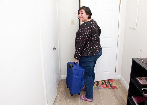 A woman opens her front door and leaves with a suitcase and a smile 