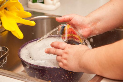 Close view of hands and a dishrag washing a bowl and glass dish in the sink 