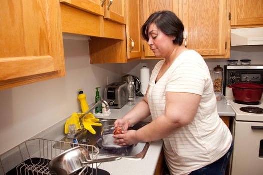  A lovely latina woman washes a glass dish in her kitchen at home 